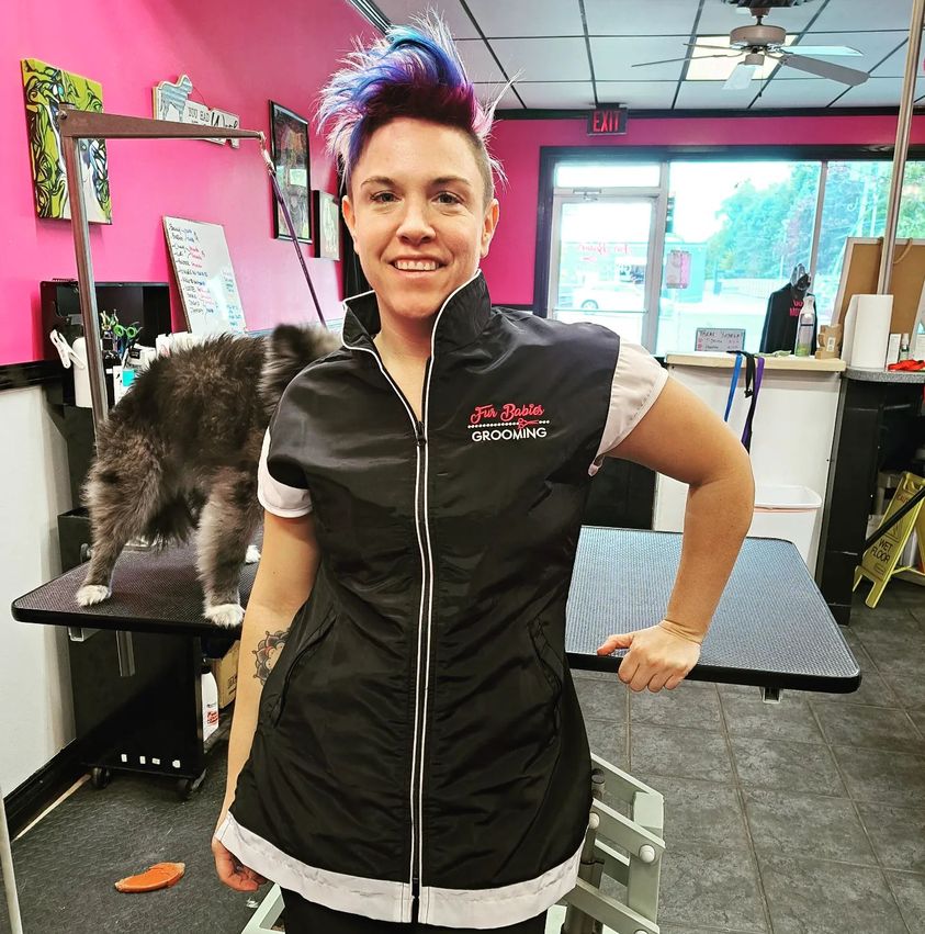 Pet groomer showing off her Black Cap Sleeve smock with custom print on it and dog in background.. it.