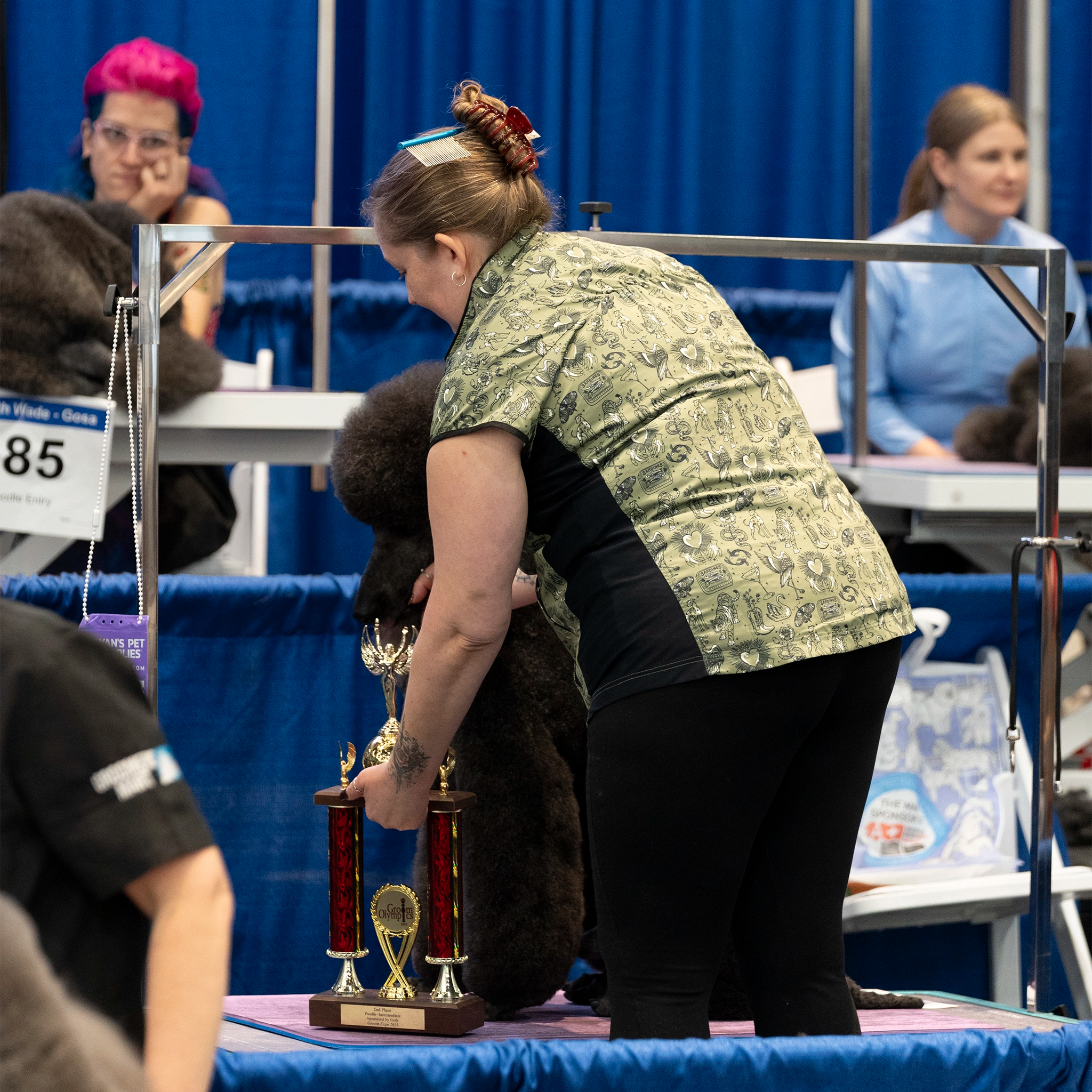 Person with a dog at a dog show, with trophies on a table